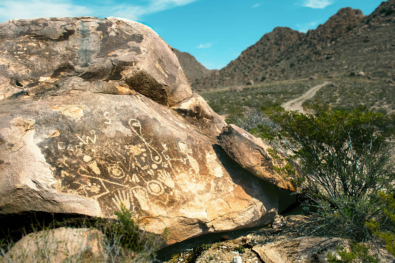 A boulder etched with Native American petroglyphs sits before a stunning mountain range.